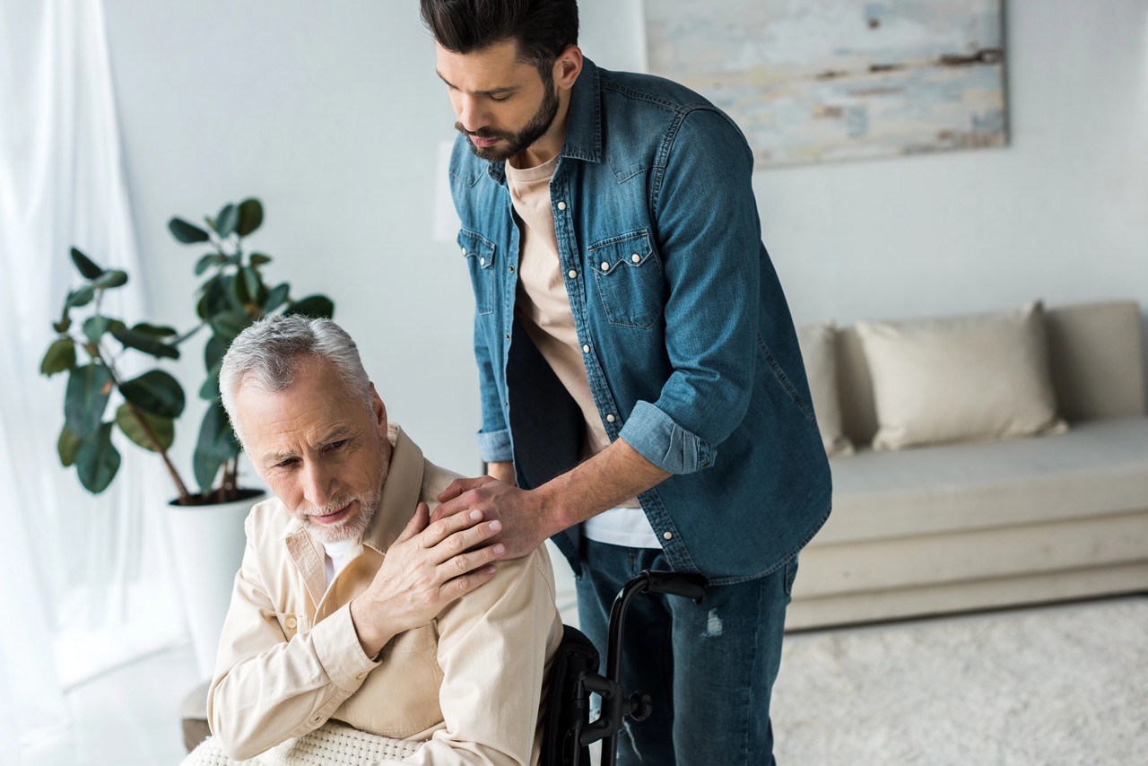 Male support worker placing a comforting hand on an elderly man's shoulder in a home care setting