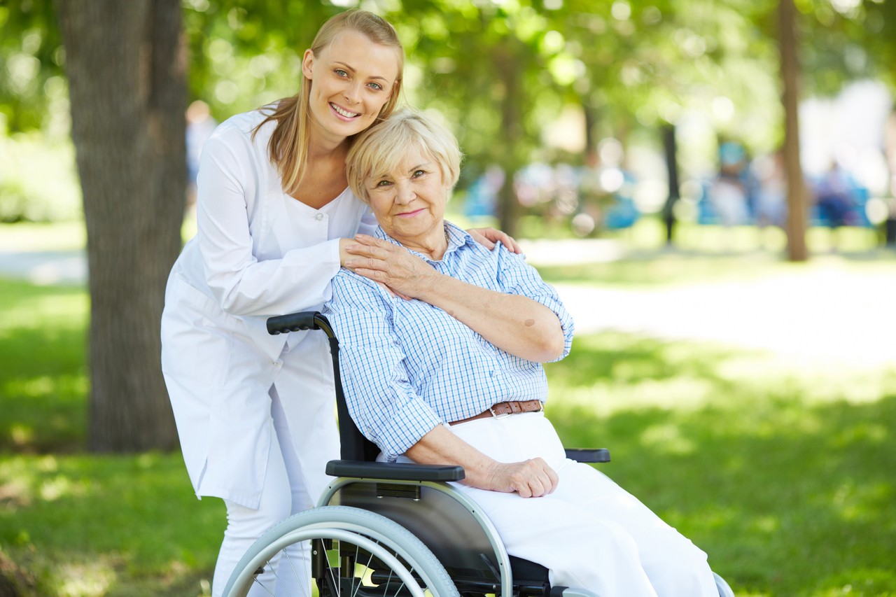 Aged care worker smiling with elderly woman in wheelchair in a sunny park setting
