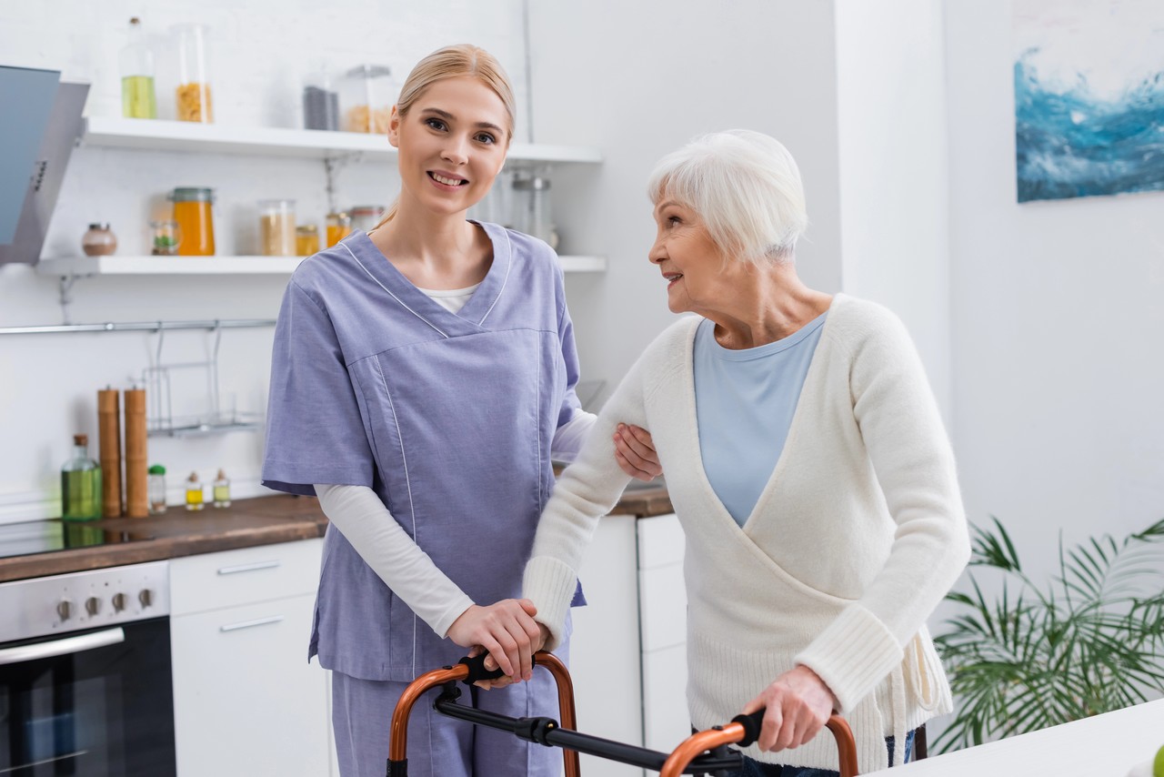 Aged care worker in uniform assisting an elderly woman using a walking frame in a home care setting