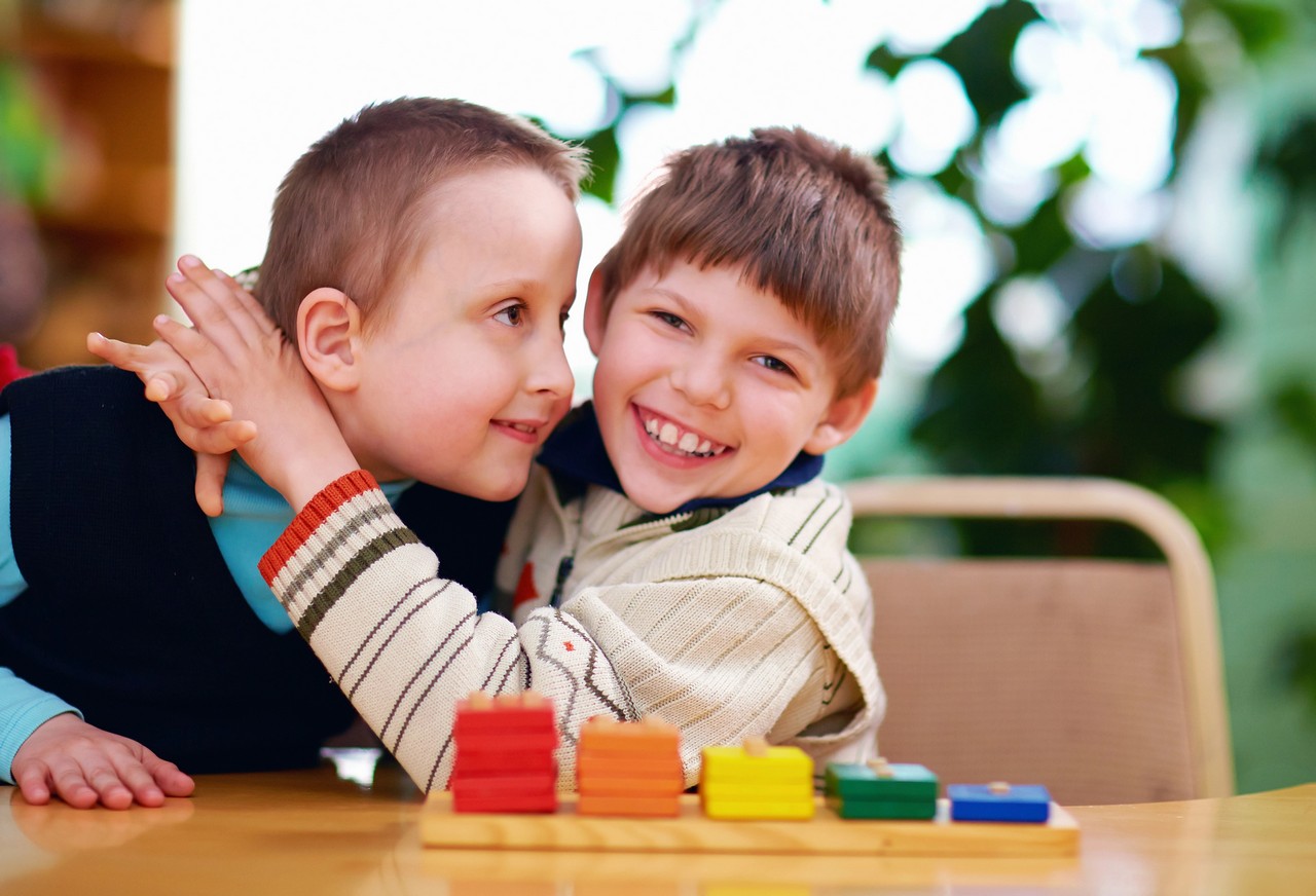 Two young boys with special needs laughing and playing with colourful building blocks in a learning environment