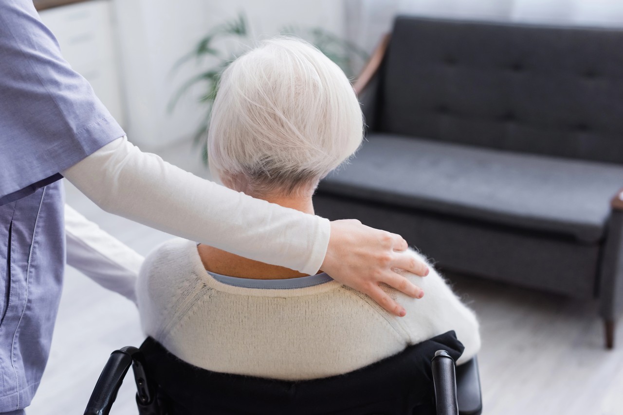 Carer placing a supportive hand on an elderly woman's shoulder in a residential care setting