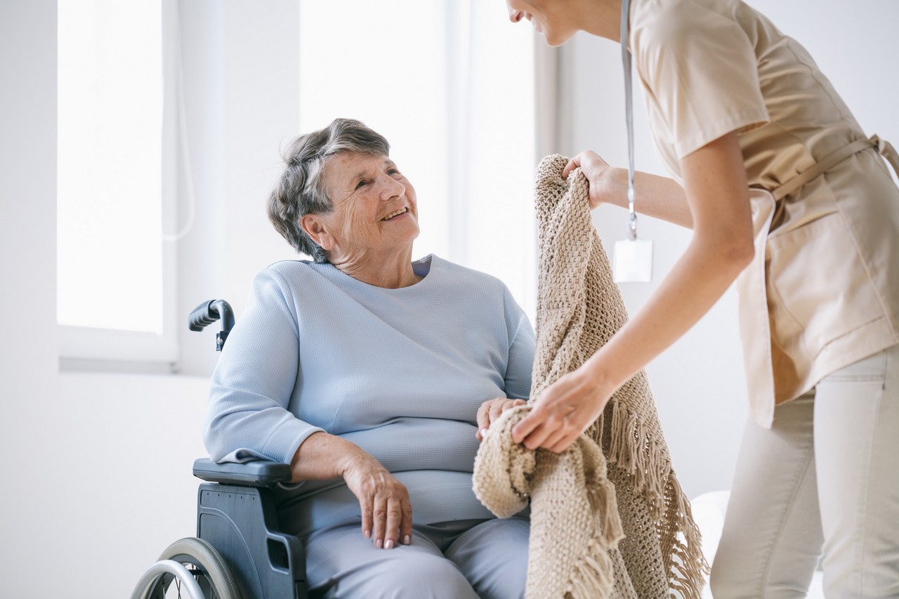 Carer attentively placing a blanket over an elderly woman in a wheelchair during vocational placement at a care facility