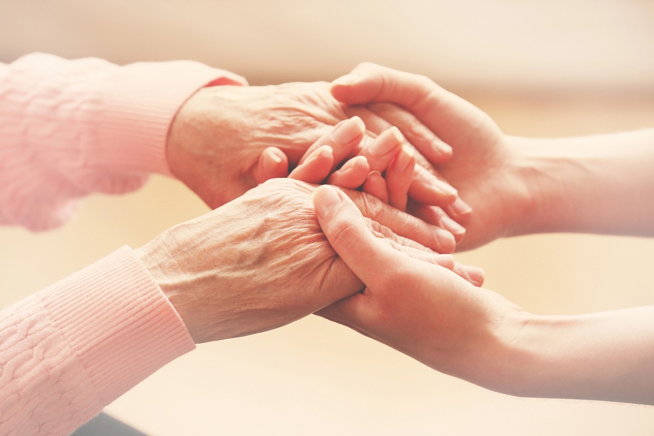 Close-up of a carer gently holding an elderly person's hands, symbolising compassionate aged care support