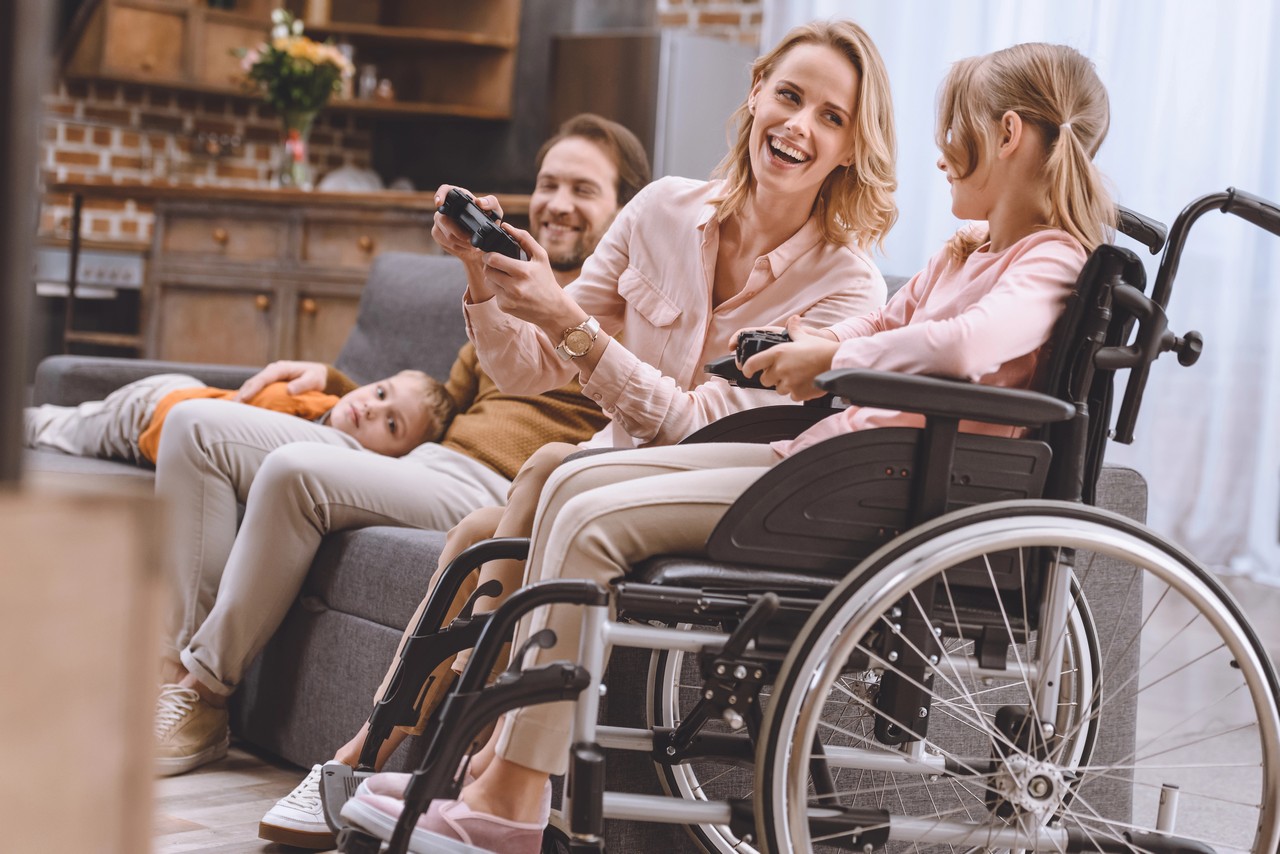 Family enjoying video games together with a young girl in a wheelchair, demonstrating disability inclusion at home