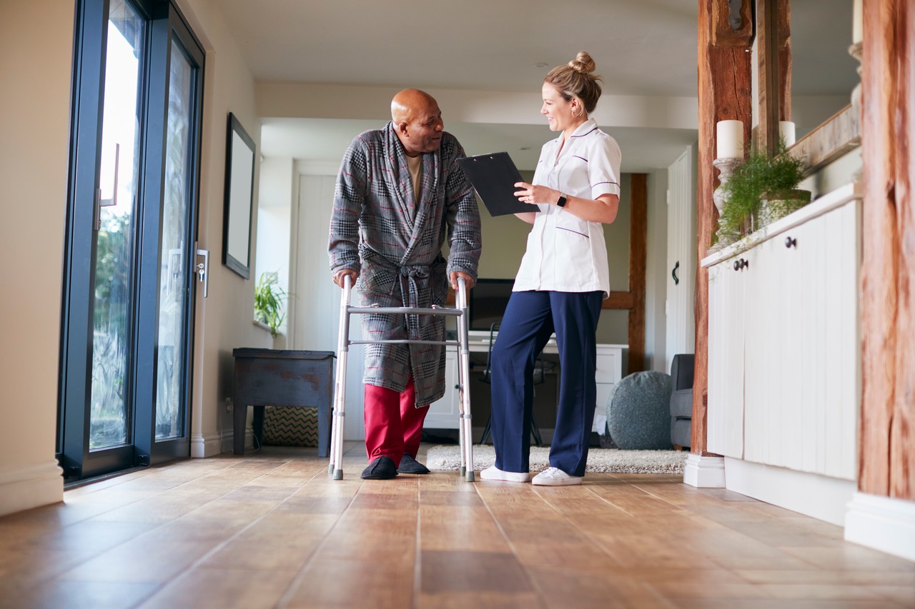 Home care nurse reviewing care plan with elderly man using a walking frame in his home