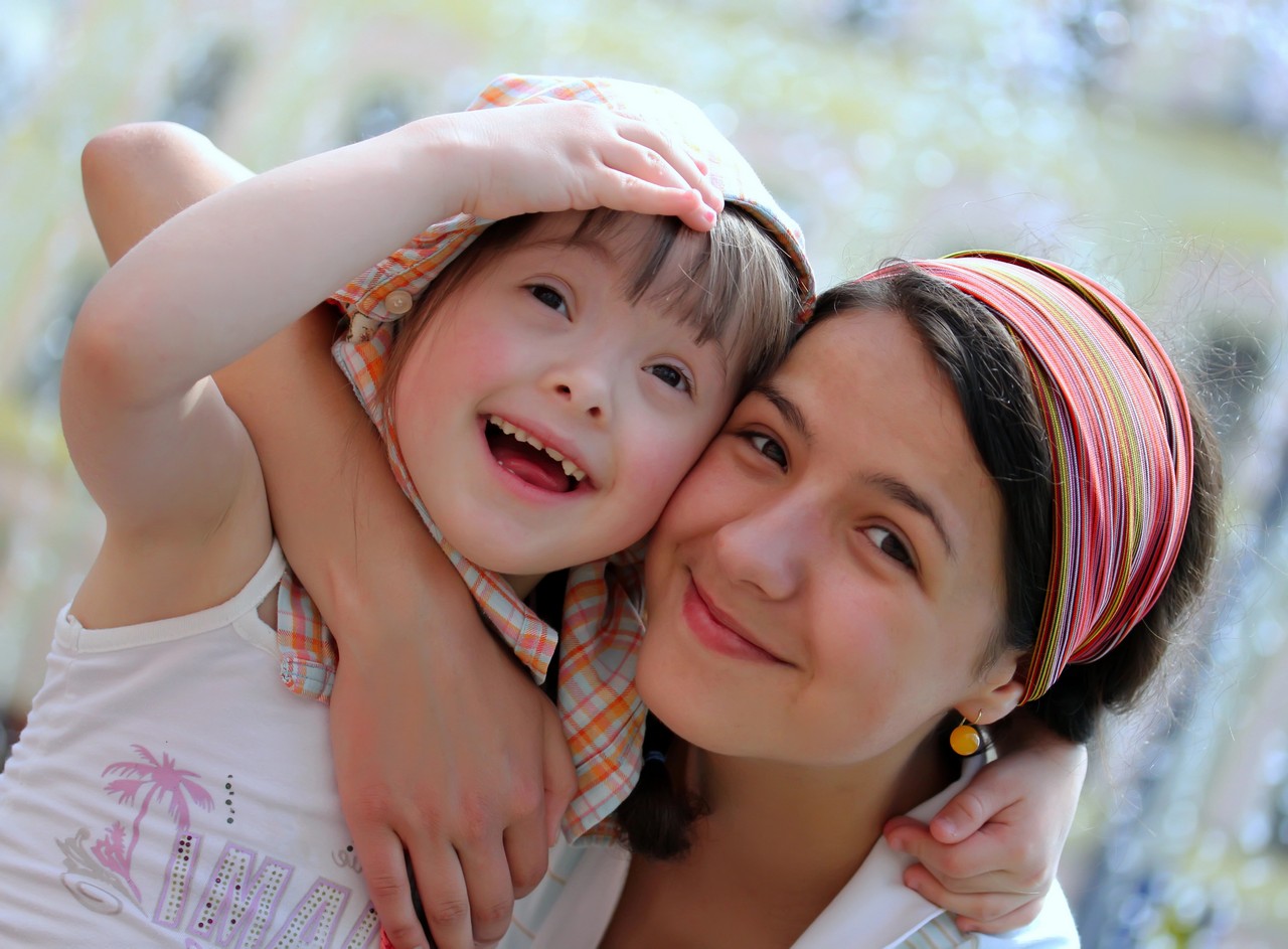 Mother warmly embracing her young daughter with Down syndrome outdoors in a sunlit setting