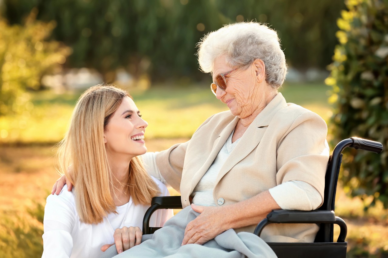 Young carer sitting with elderly woman outdoors at sunset, representing the human connection central to community services training