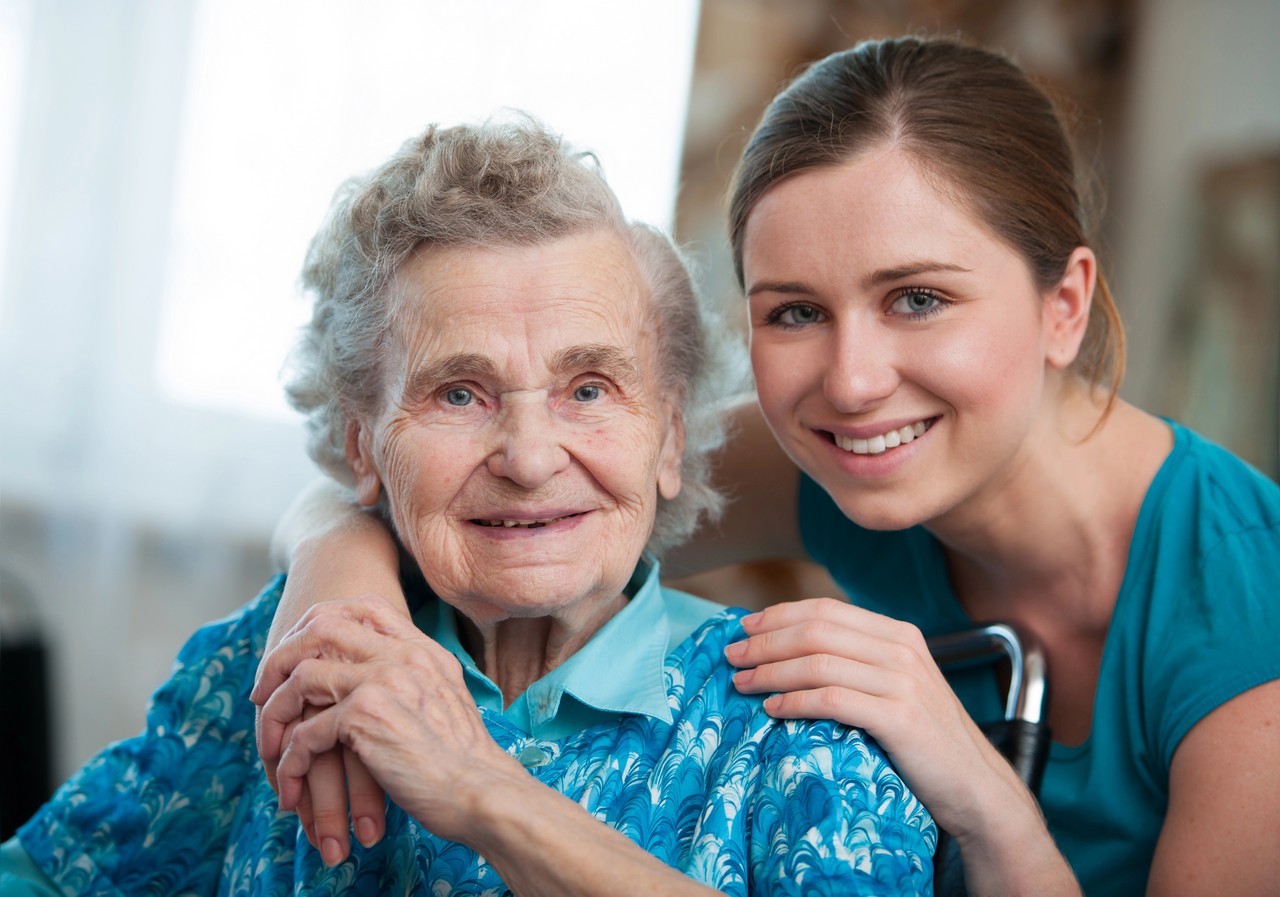 Young carer smiling warmly alongside an elderly woman she supports, representing the human connection in community services training
